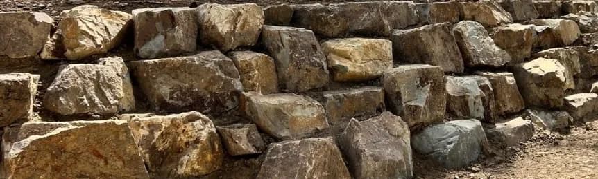 Coldstream stone retaining wall in tan, gold, grey and blue, dry-stacked along a driveway by Rock'n Earthworks