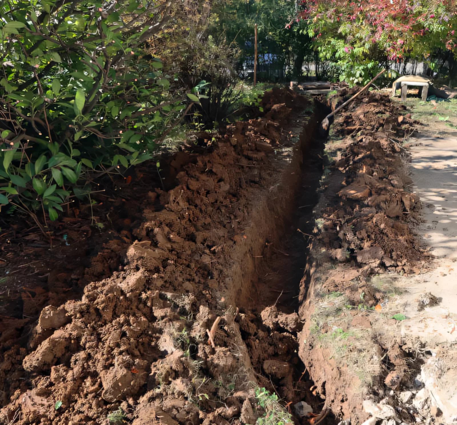 Freshly dug drainage trench cutting through a garden bed, ready for pipe and gravel by Rock'n Earthworks