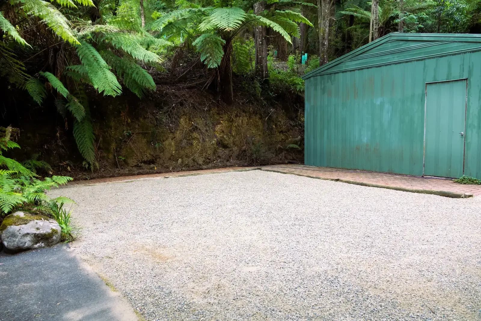 Completed gravel driveway with teal shed against steep fern-covered hillside