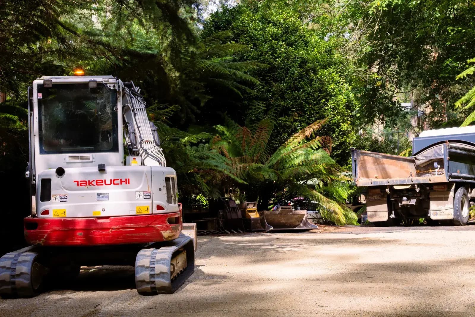 Takeuchi TB257FR excavator with bucket attachments and tipper truck on a crushed rock site surrounded by tree ferns