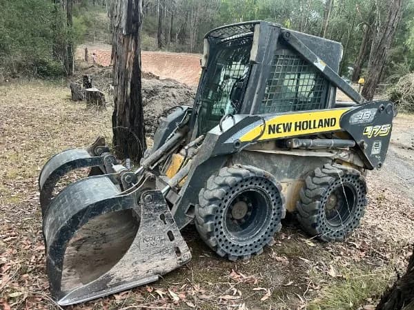 New Holland L175 skid steer with grapple bucket on a forested job site