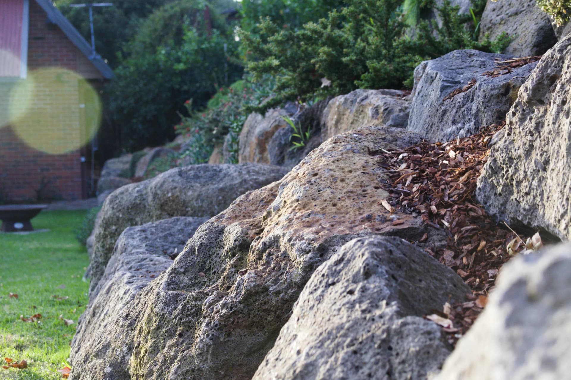 Side-lit row of boulders showing the locked-in placement of stones along a sloped lawn, built by Rock'n Earthworks